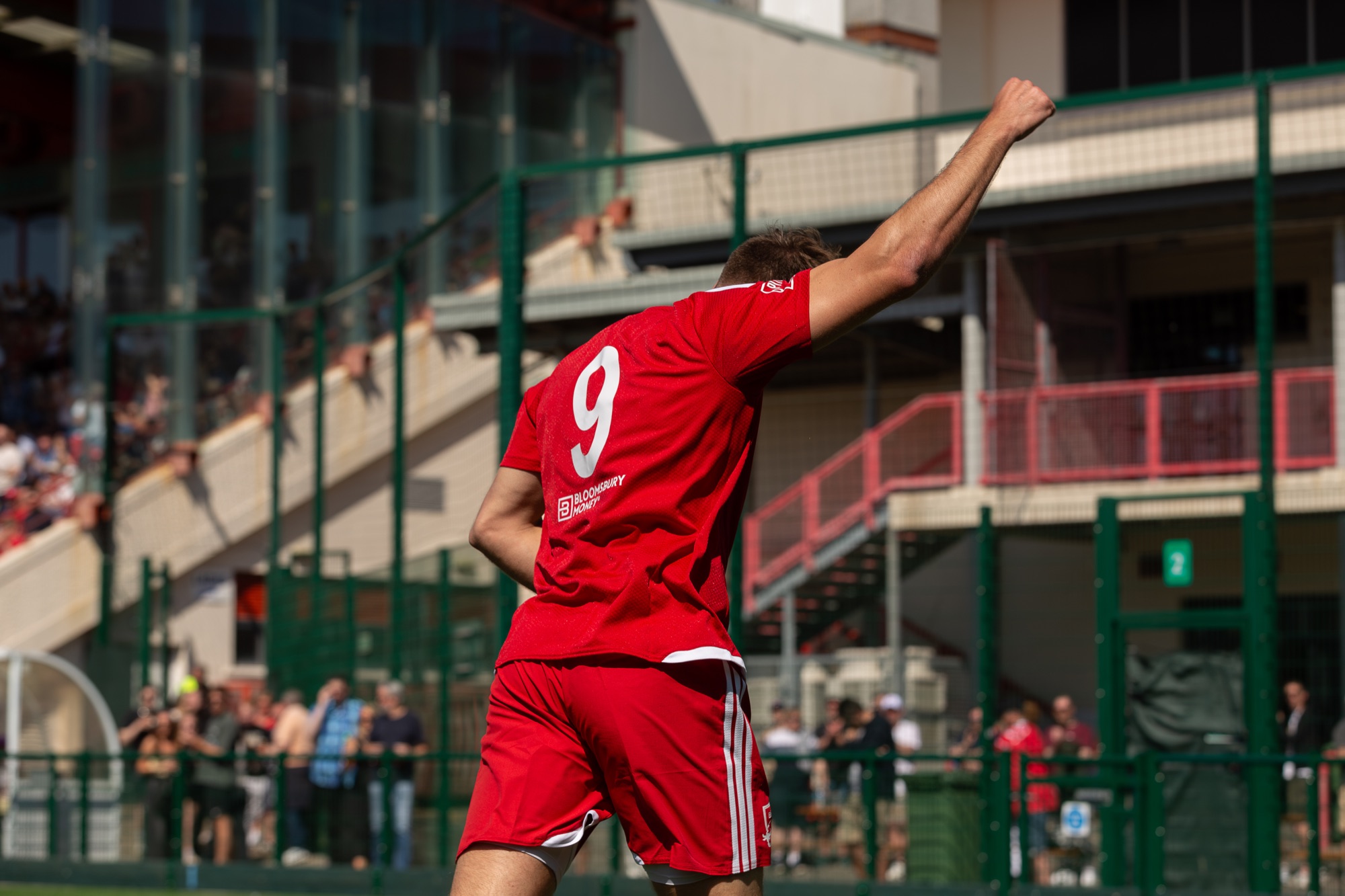 A Jersey Bulls player celebrating in the red home strip at Springfield